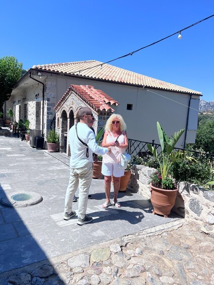 Two people standing on a stone-paved path in front of a building with a tiled roof. 2
