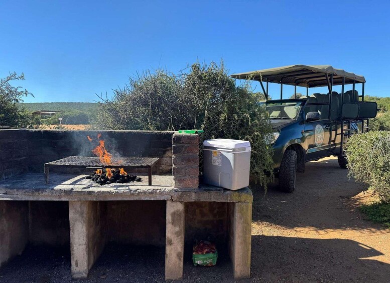 A portable grill with flames, a cooler, and a vehicle in a rural setting. 3