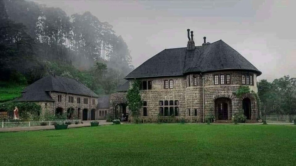 A large stone building with a circular tower, surrounded by a well-maintained lawn and trees. 3