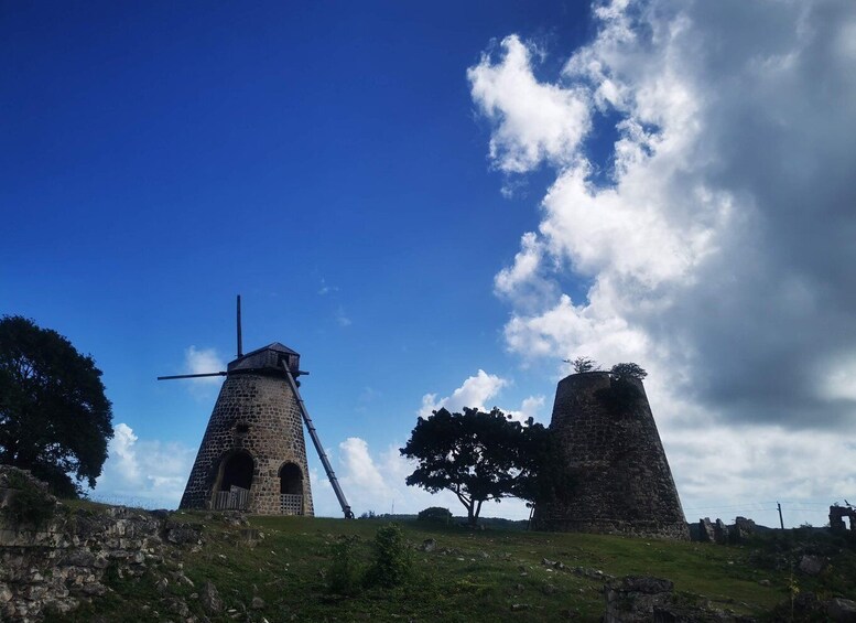 A windmill and a stone tower on a grassy hill under a blue sky with clouds. 5