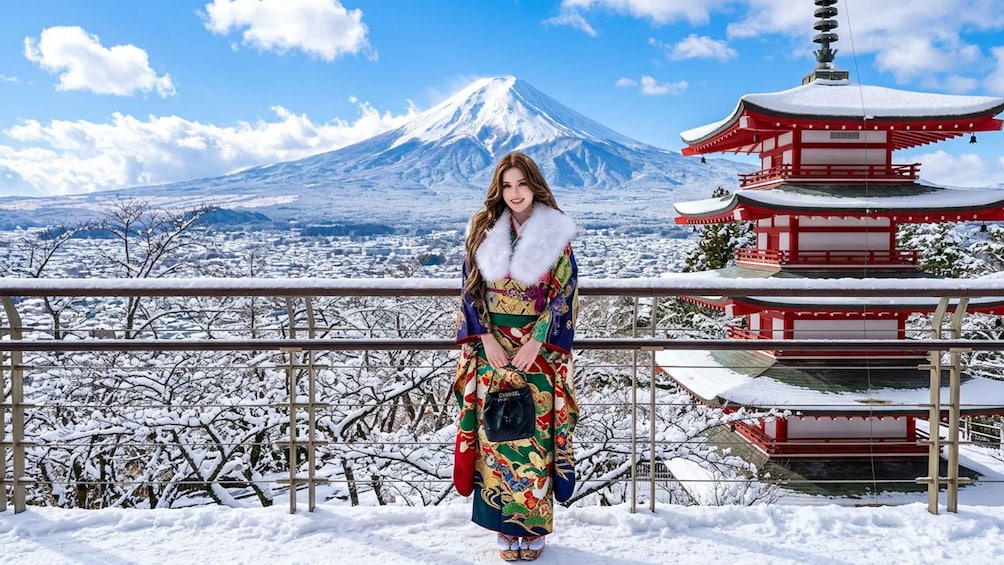 A person in traditional attire standing in a snowy landscape with a snow-covered pagoda and Mount Fuji in the background. 1