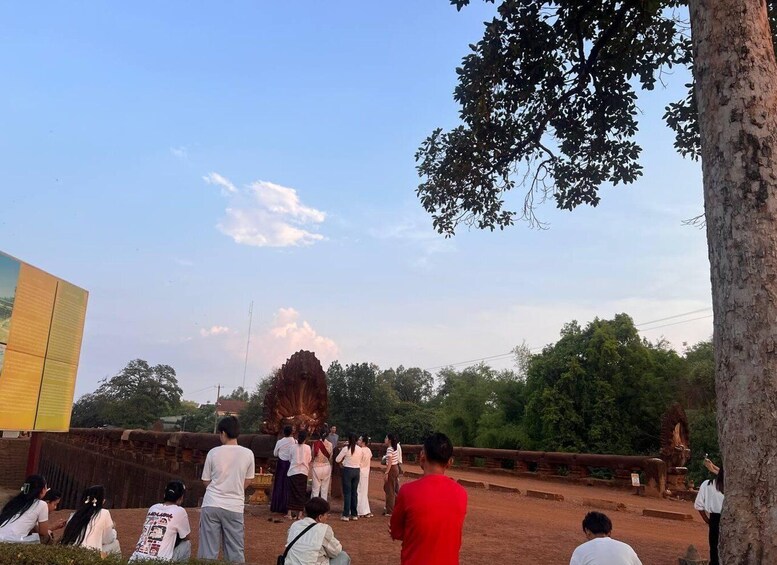 A group of people observing a large, ornate statue in a natural setting with trees and a clear sky. 3