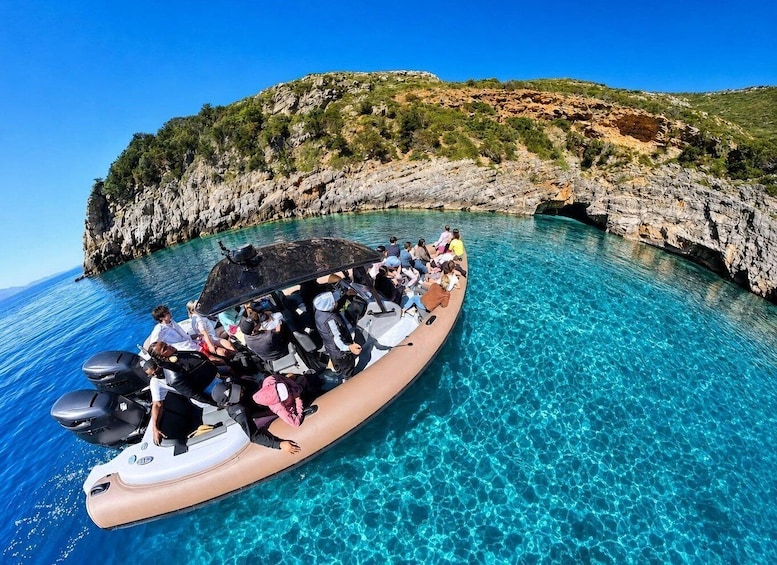 A boat with people on a clear blue sea, surrounded by rocky cliffs. 1