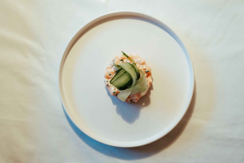 A white plate with a sushi roll topped with cucumber and a creamy sauce. 5