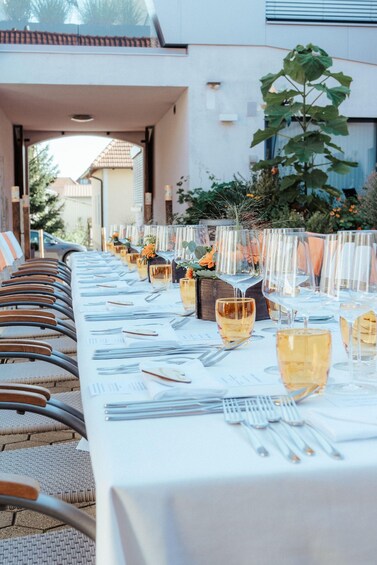 A long dining table set outdoors with chairs, glasses, and cutlery. 1