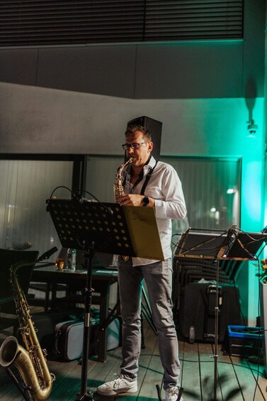 A person playing a saxophone in a room with musical instruments and sheet music stands. 3