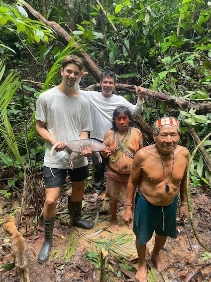 Four people in a forested area, one holding a snake, another holding a branch, and a third wearing traditional attire. 4