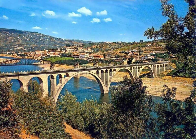 A stone bridge with multiple arches over a river, surrounded by greenery and a town in the background. 5