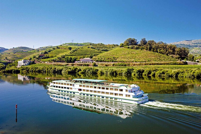 A river cruise boat on a calm river with green hills and a clear sky in the background. 1