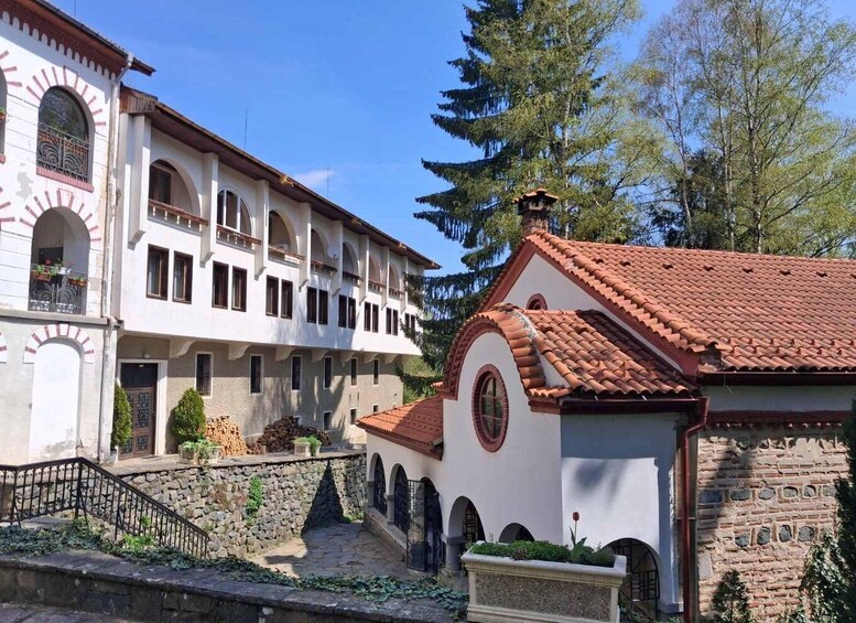 A historic building with arched windows and a red-tiled roof, surrounded by stone walls and greenery. 5