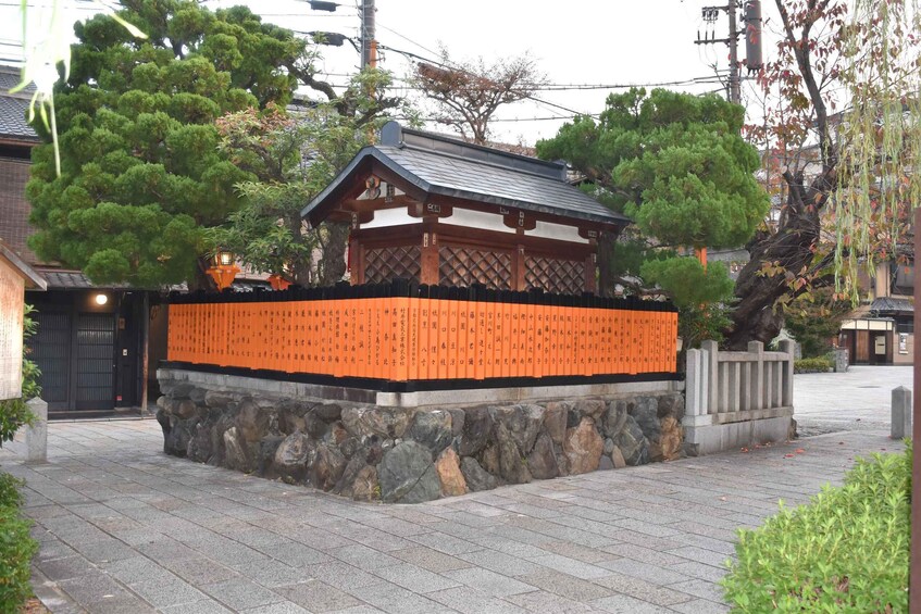 A traditional Japanese shrine with a stone base, wooden structure, and orange plaques. 2