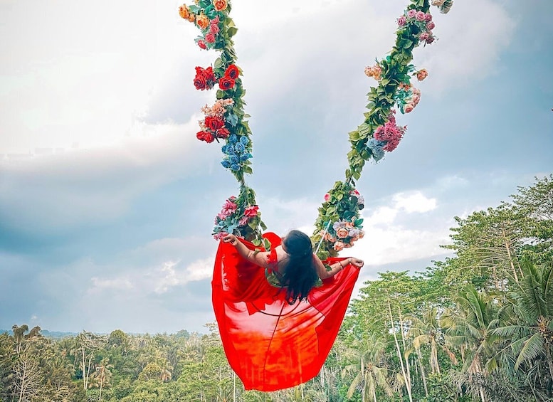 A person swinging on a red swing decorated with flowers against a backdrop of palm trees and a cloudy sky. 5