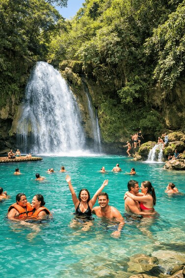 A waterfall, clear turquoise water, and people swimming and enjoying the natural setting. 5