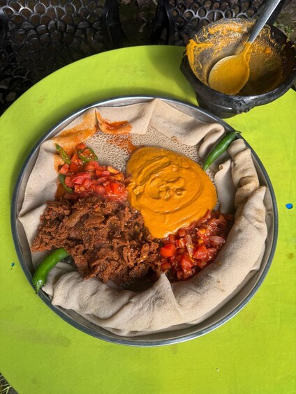 A meal with injera, a red spicy mix, a yellow sauce, and a dark meat dish on a green table. 2