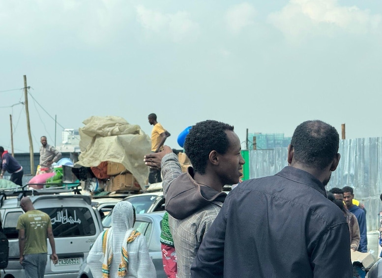 A crowded street with people carrying goods, a parked car, and a building in the background. 3