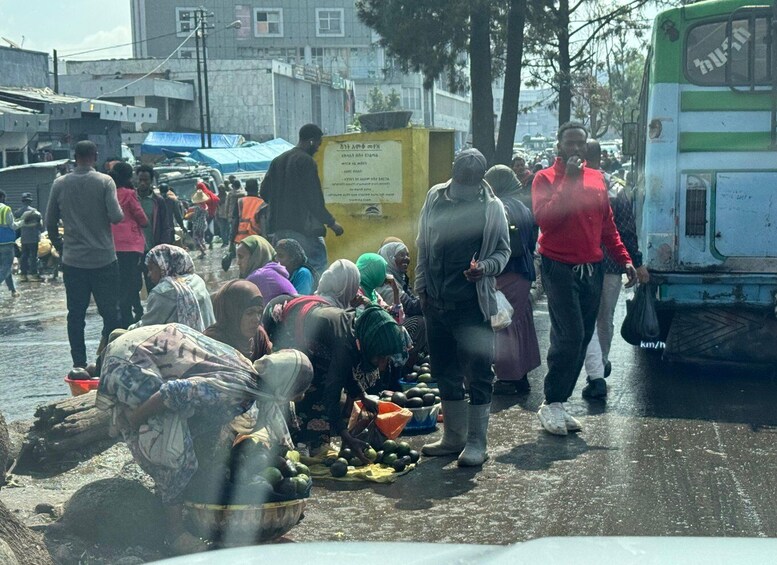 A busy street market with people selling and buying goods, a bus, and buildings in the background. 5