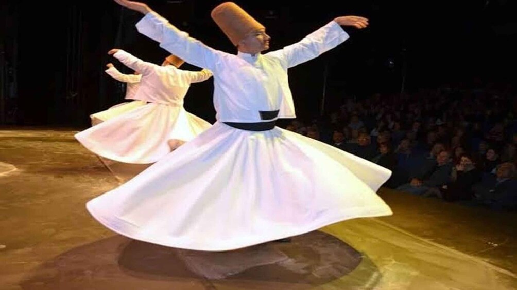 A person performing a dance with a flowing white skirt on a stage. 3