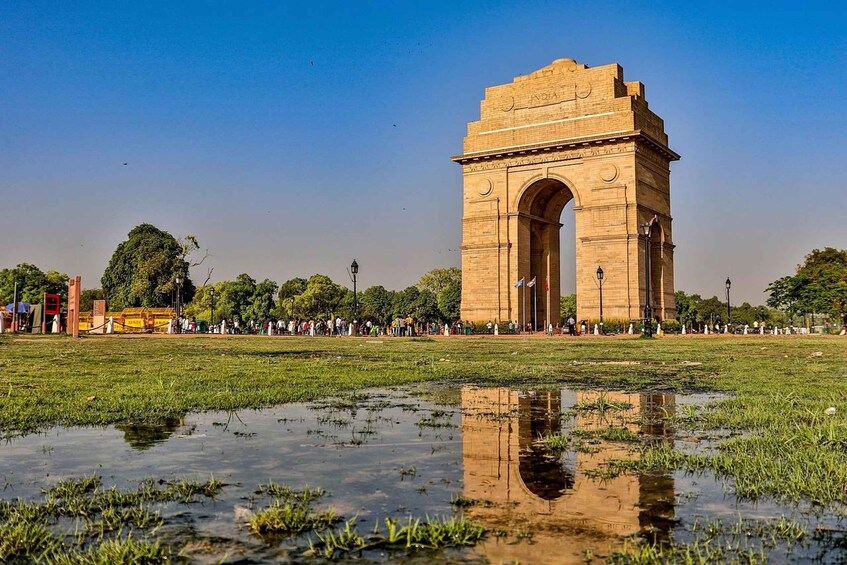 The India Gate in New Delhi, surrounded by a grassy field with a puddle reflecting the structure. 3