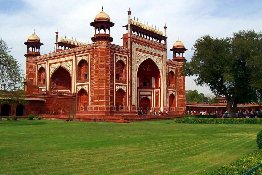 A large, historic building with multiple domes and arches, surrounded by a well-maintained lawn and trees. 3