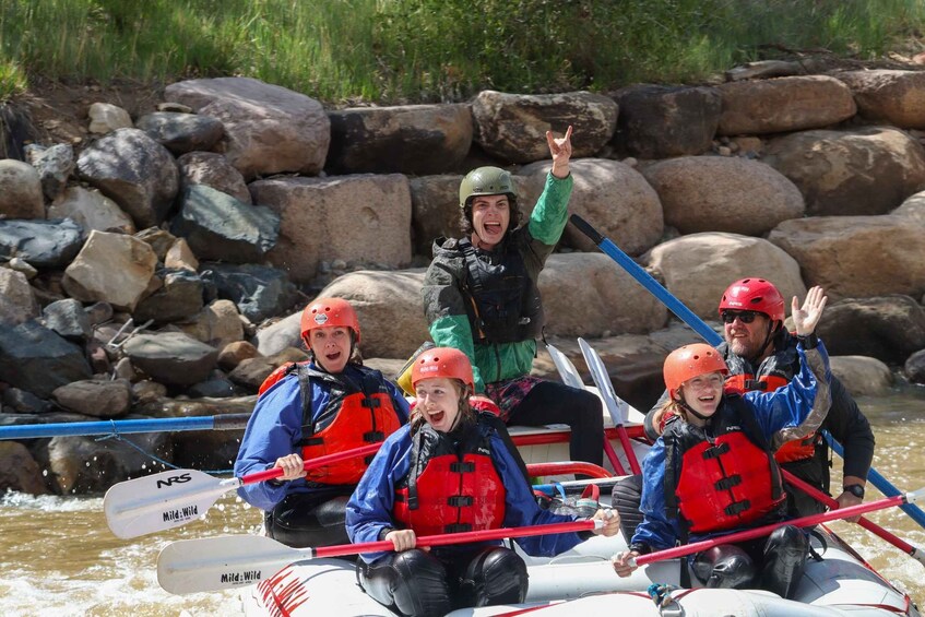 A group of people in a raft on a river, wearing life jackets and paddles. 1