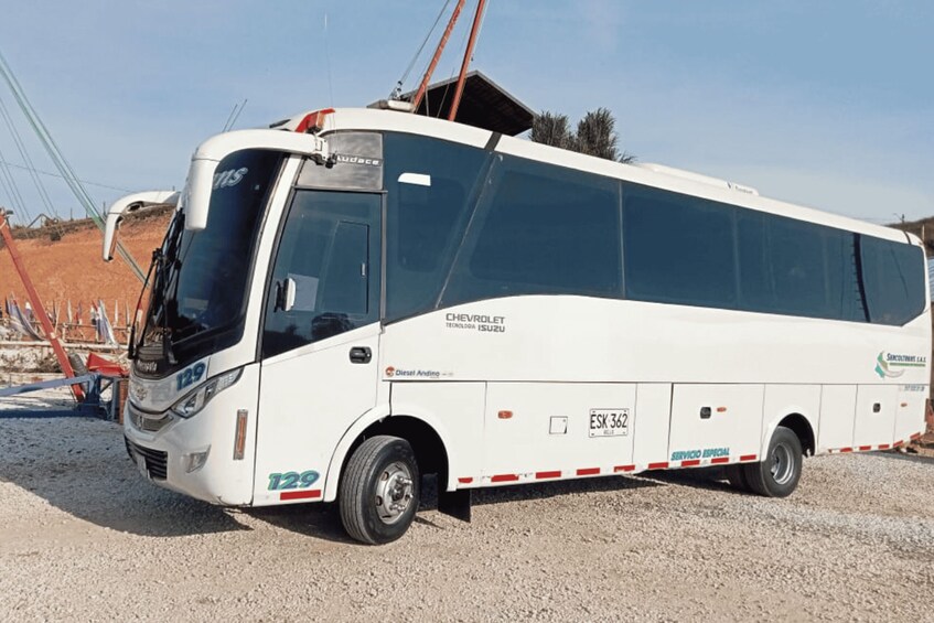 A white Chevrolet Isuzu bus parked on a gravel surface. 1
