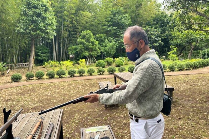 A person holding a rifle in a park with trees and benches. 5