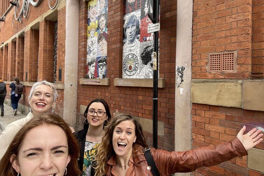 Un gruppo di persone che si fa un selfie davanti a un edificio con una facciata in mattoni e un murale. 1