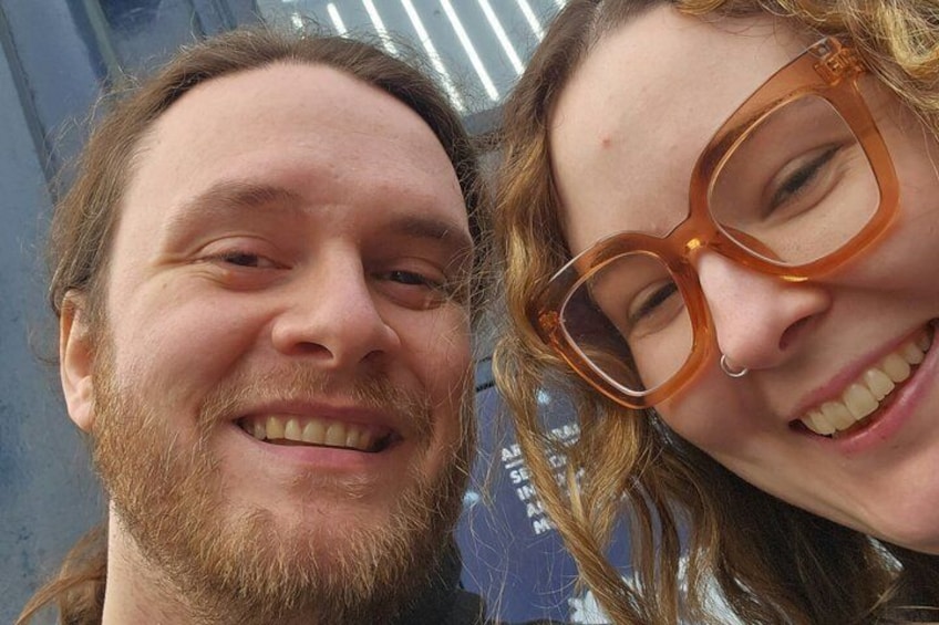 Due persone con gli occhiali, una con la barba, davanti a un edificio con facciata blu e bianca. 4
