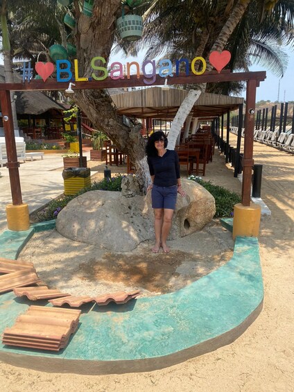 A person standing under a sign that reads 'BLSangano' with a palm tree and beach chairs in the background. 5