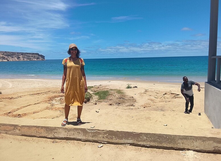 A person standing on a sandy beach with a clear blue sky and calm sea in the background. 4
