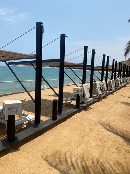 A beach with a wooden walkway, white lounge chairs, and a metal railing. 1