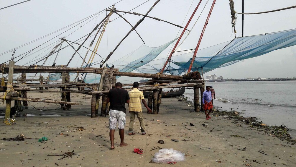 A fishing net structure on a sandy beach with people around it. 2