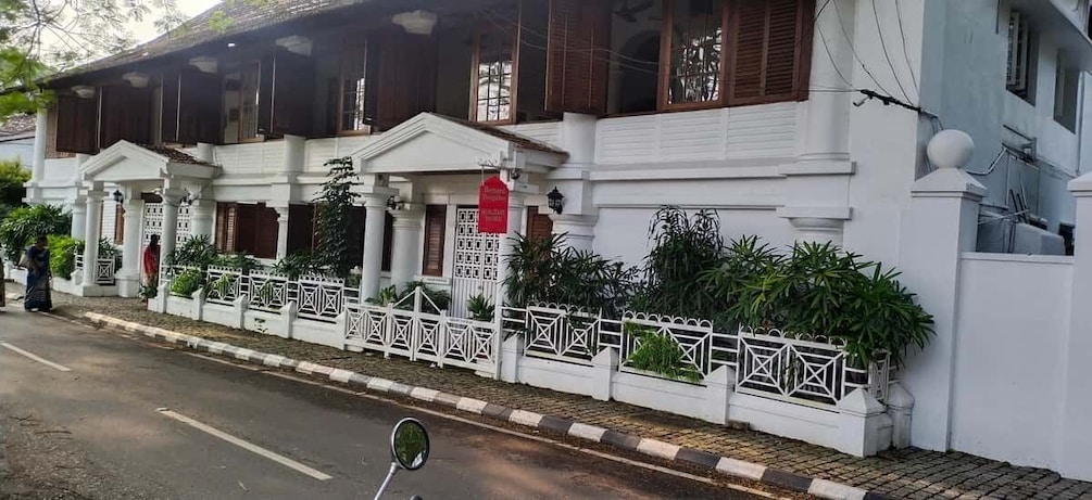 A white colonial-style building with wooden shutters, a white picket fence, and lush greenery. 5