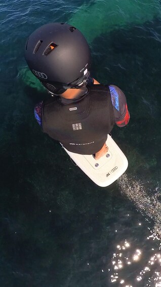 A person wearing a helmet and a life jacket on a surfboard in clear water. 5