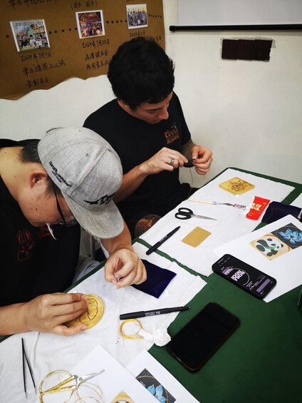 Two people working on a craft project with various materials and tools on a table. 3