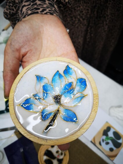 A hand holding a wooden tray with a blue and white flower design. 1