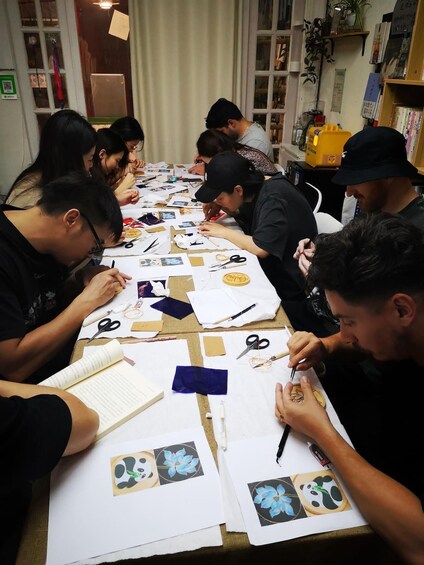 People engaged in a craft activity, working with paper, scissors, and glue at a table. 2