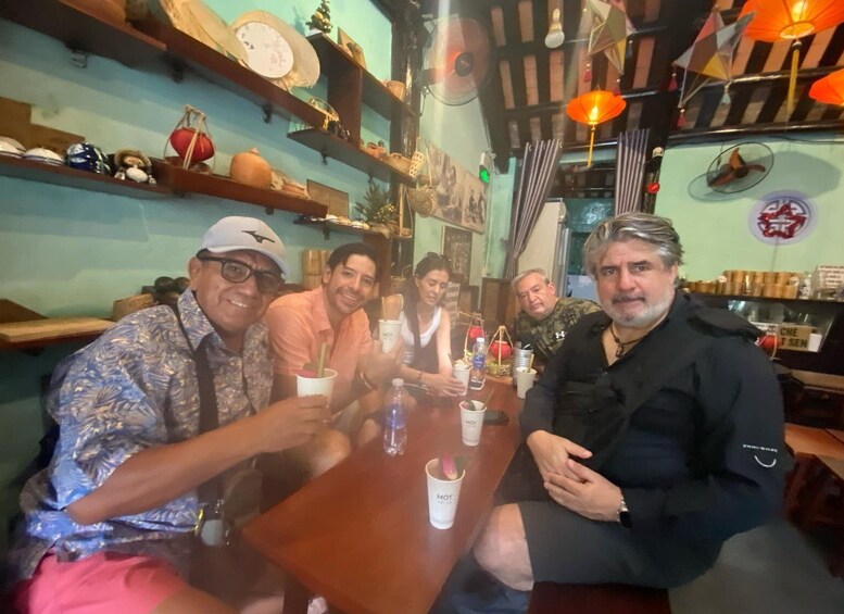 A group of people sitting at a wooden table in a restaurant with shelves of dishes and a clock on the wall. 2