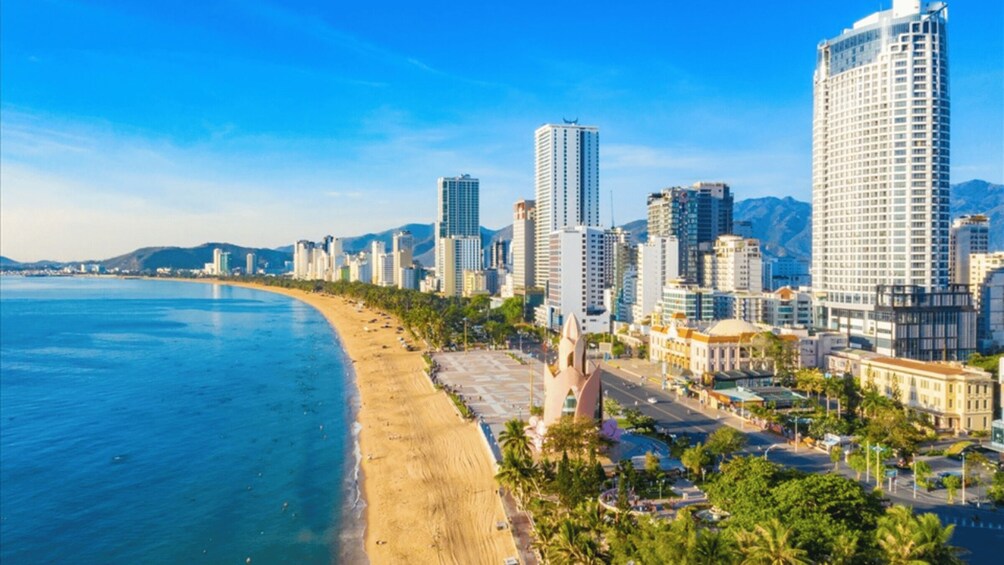 A coastal cityscape with a beach, high-rise buildings, and mountains in the background. 1