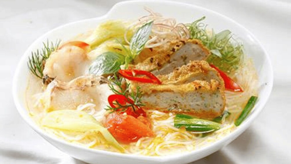 A bowl of noodle soup with vegetables and a piece of chicken. 3