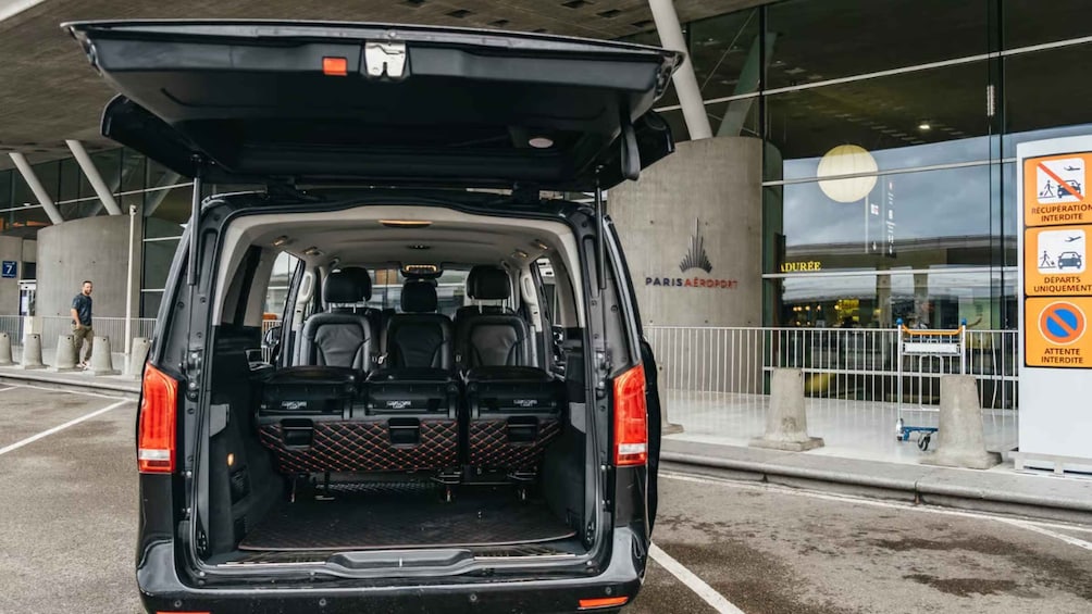 The back of a van with its trunk open, parked in front of an airport terminal. 4