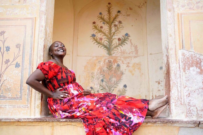 A woman sitting on a ledge with a floral mural in the background. 1