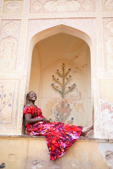 A woman in a colorful dress sitting in a doorway with floral wall decorations. 5