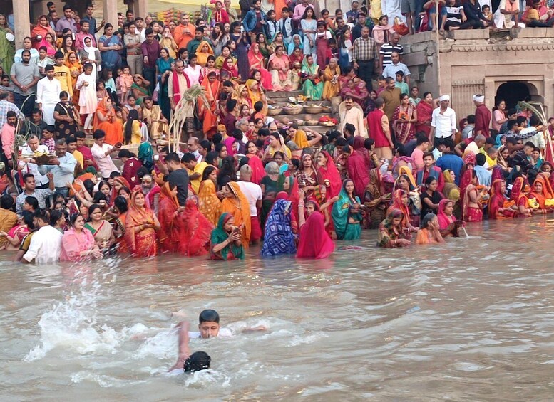 A large crowd of people in traditional attire gathered by a river, some standing on steps and others in the water. 3