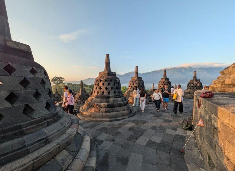 A group of tourists at a historical site with stone structures and a mountainous backdrop. 3