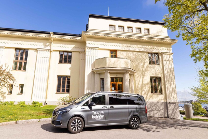 A silver minivan parked in front of a cream-colored building with classical architecture, including columns and a portico. 5