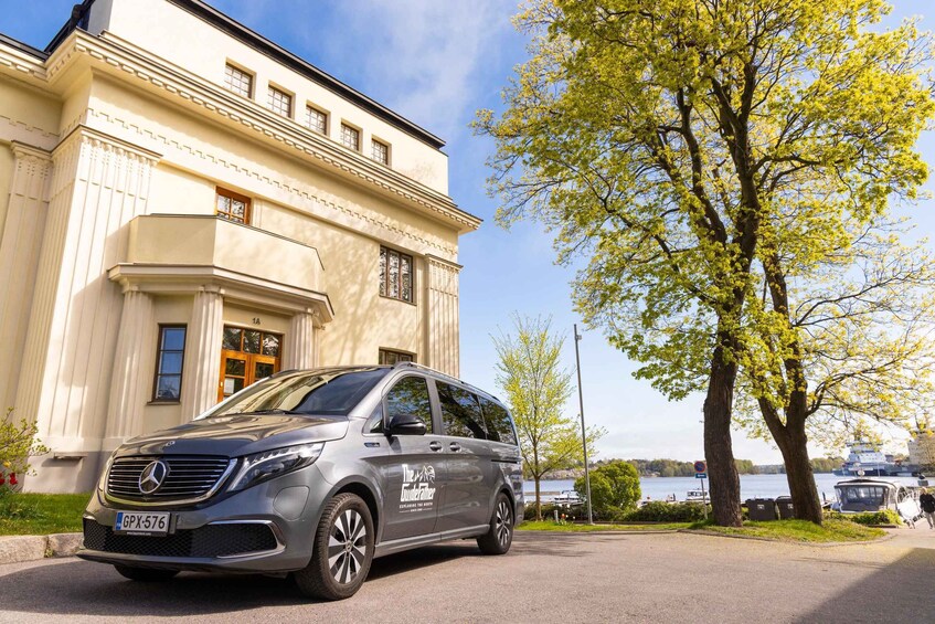 A silver Mercedes-Benz van parked in front of a classical building with a tree and a body of water in the background. 3
