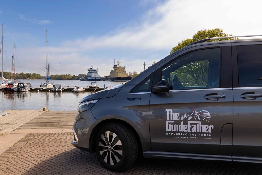 A van parked by a marina with boats and a large ship in the background. 4