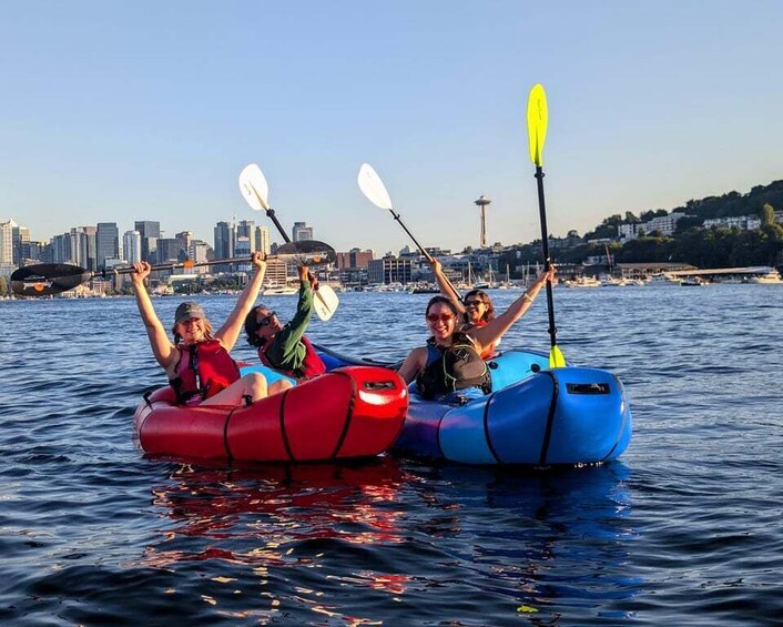 People kayaking in inflatable rafts on a body of water with a city skyline in the background. 1