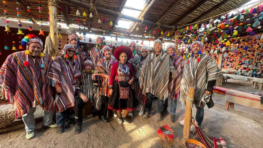 A group of people in traditional attire with colorful decorations hanging from the ceiling in a rustic indoor setting. 1